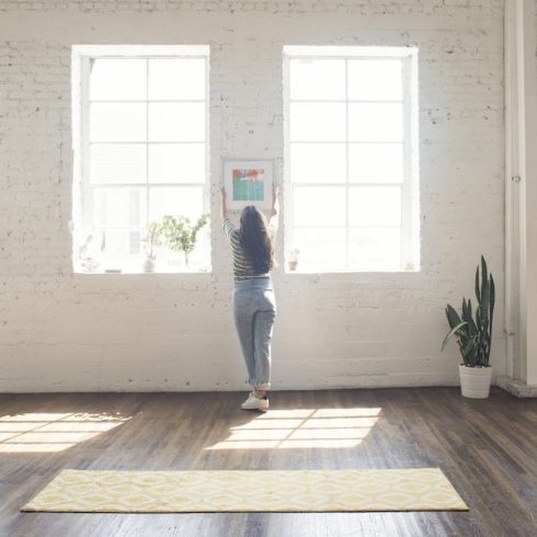 woman attaching picture frame to white brick wall in a loft