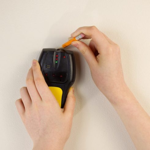 hands using stud finder on beige wall