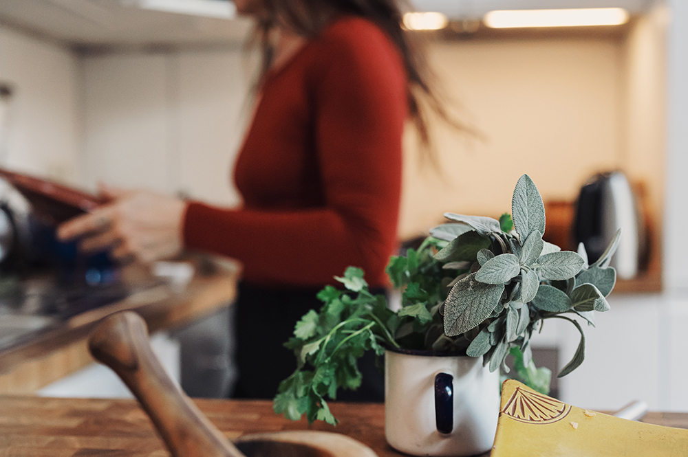 Person cooking in kitchen with a small pot of herbs in the foreground