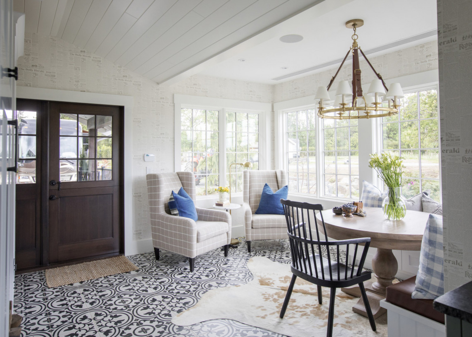 windowed eating nook beside dark brown door, two wing back chairs, round table, chair and black and white patterned floor