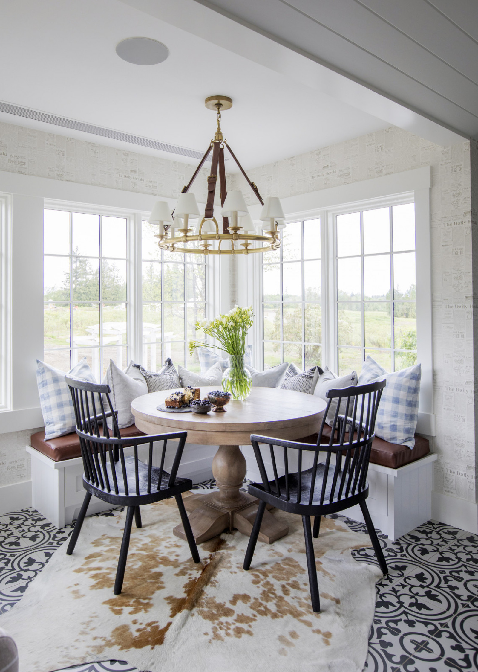 corner of windowed eating nook with built in seating, round table and two black chairs on hide rug, black and white tiled floor