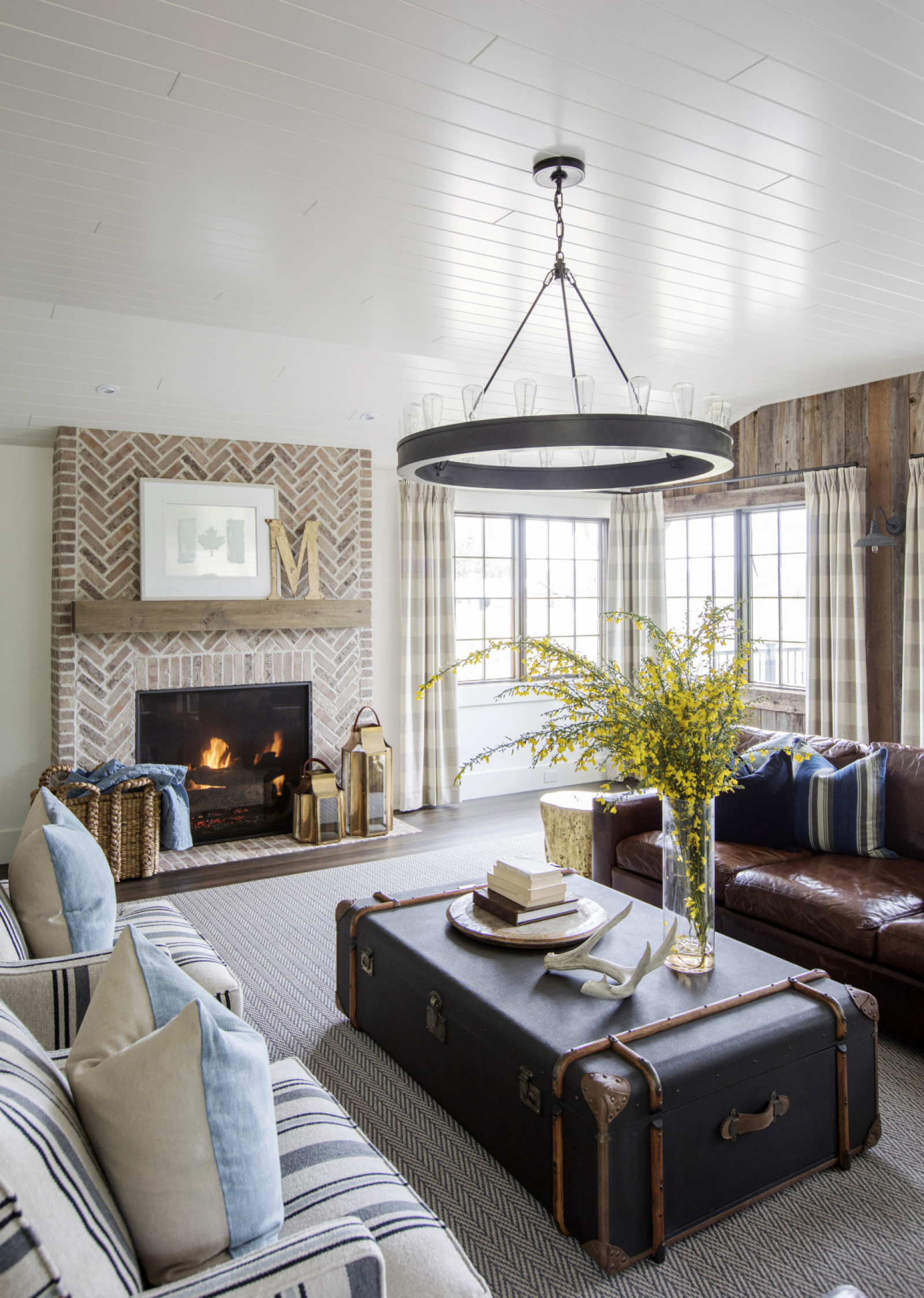 farmhouse living room with brick fireplace, chevron rug, trunk as coffee table with forsythia arrangement on top