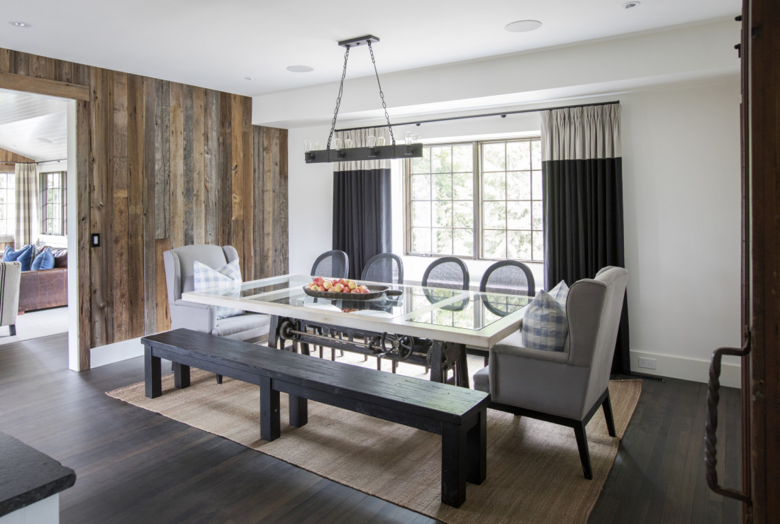 farmhouse dining room with black bench, two wing backs, four chairs, glass insert table, black drapes