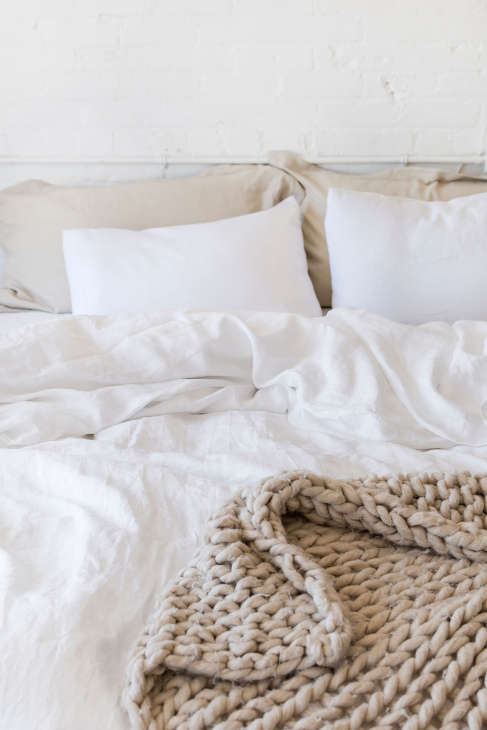 comfortable bed in white bedroom with light linen sheets