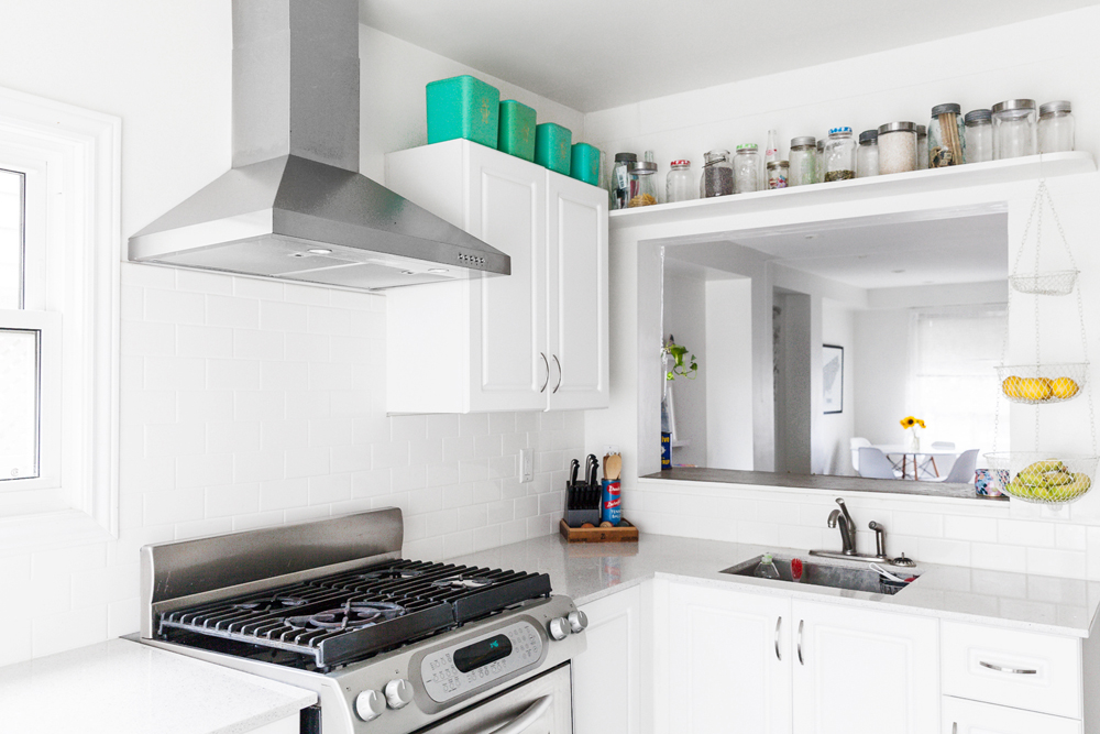 A small white kitchen with open shelving on top of the cabinets and window area