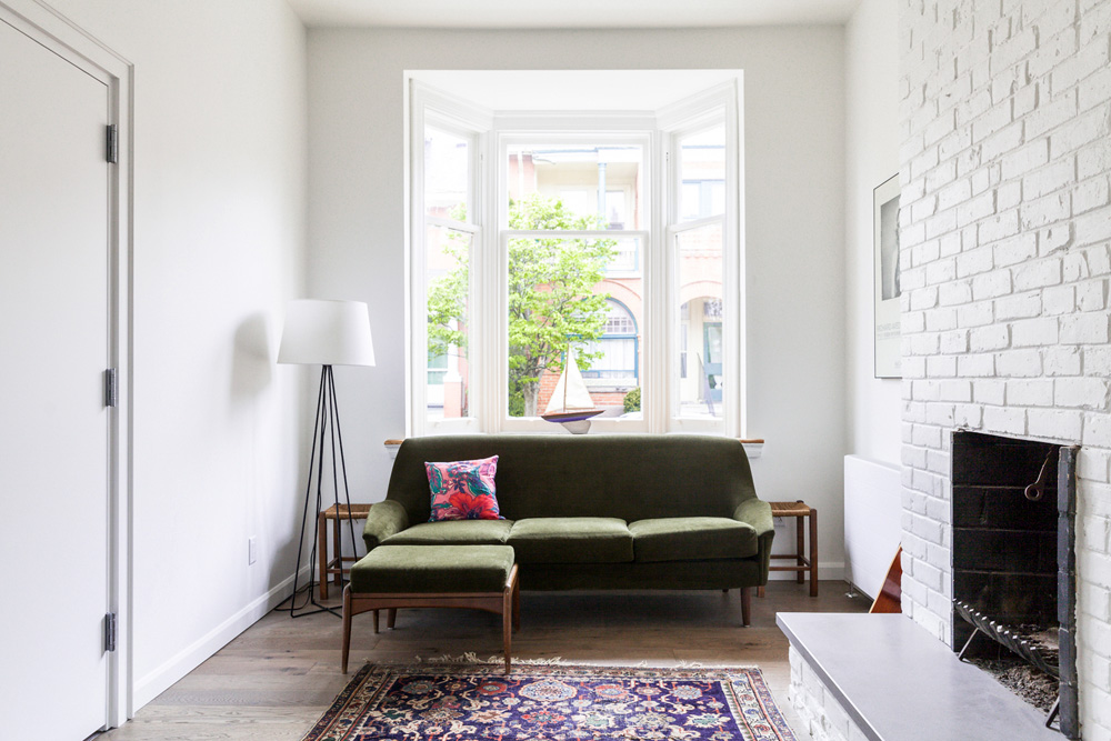 green velvet sofa in front of bay window in white room