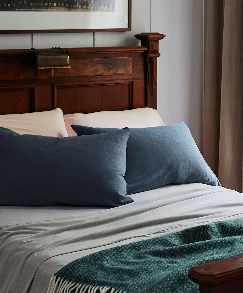 comfy bed with grey flannel sheets and assorted pillows and a blanket on top