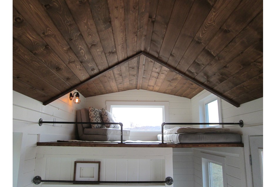 loft bed and chair in upper level of white tiny house