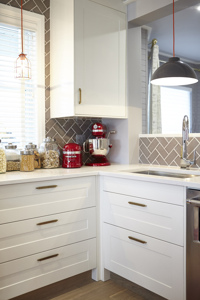 Modern kitchen with white cabinetry, brass hardware and grey tiled backsplash.