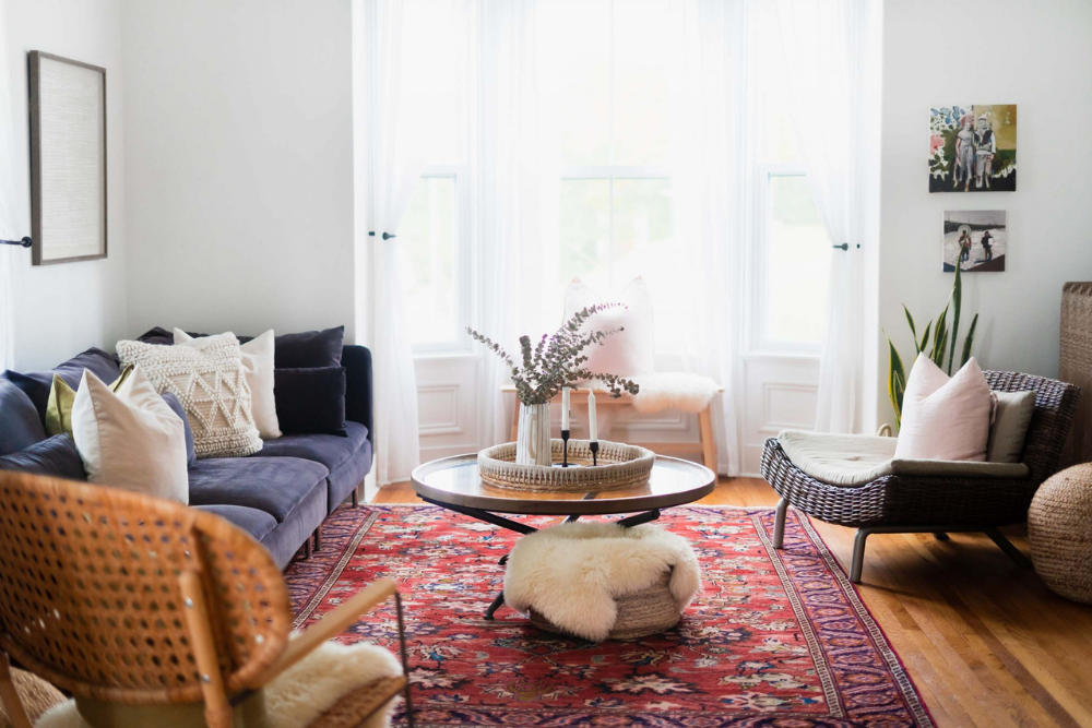 A living room featuring neutral walls, curtains and cozy textiles like cushions and furry throw blankets. Other colours are added as accents, such as a deep red Persian rug and a navy blue couch.