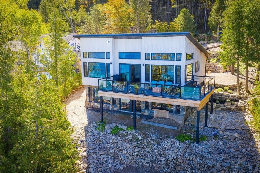 A modern and sleek birds eye view of a white luxury cottage with lots of windows.