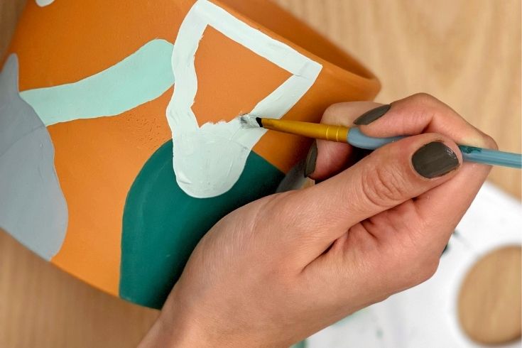 Someone hand painting a terracotta clay pot