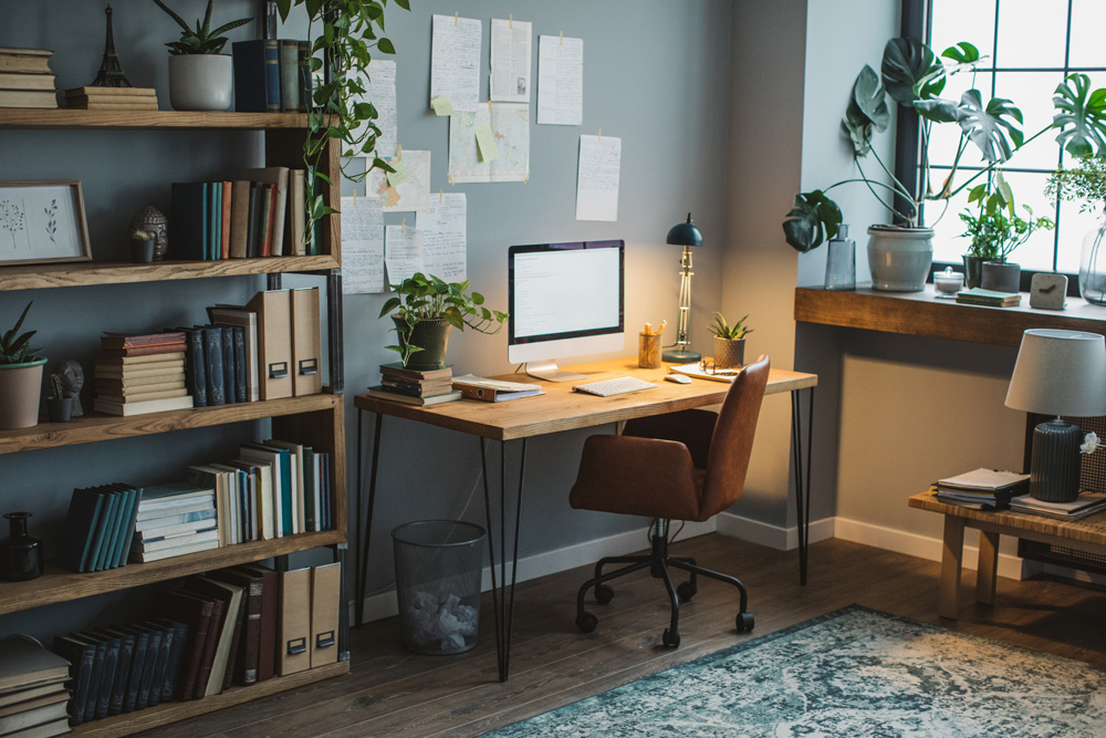 A home office with calming grey walls and wooden touches via the floorboards, windowsill, bookshelf, desk and low bench.