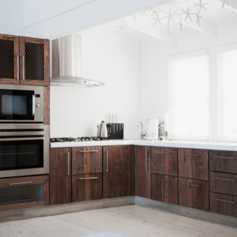 A stylish, spacious kitchen with natural dark wood cabinetry, bright white walls and large, airy windows.