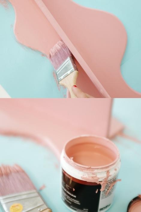 A person painting a wavy wooden shelf pink 