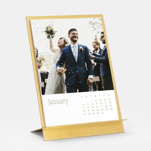 A brass easel and calendar with a photo of a bride and groom on their wedding day.