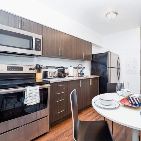 An eat-in kitchen with round table, dark wooden chairs, dark upper and lower cabinetry and stainless steel appliances