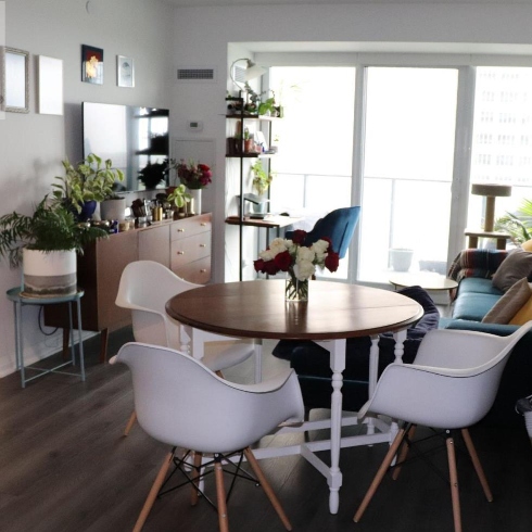 An open concept dining and living area with round table, tulip chairs, dark wooden flooring and large sliding glass balcony doors