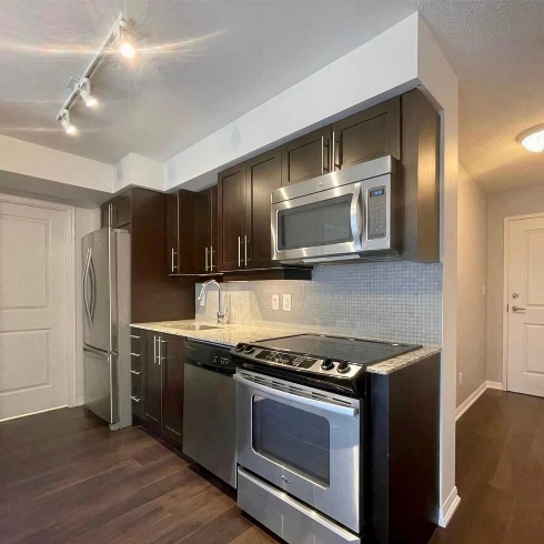 A kitchen with stainless steel appliances, dark wooden upper and lower cabinetry and dark wooden floors