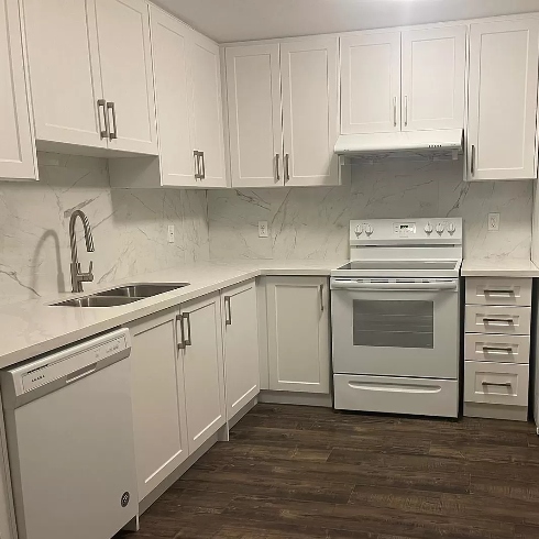 A large kitchen with upper and lower cabinetry in white and a white stove