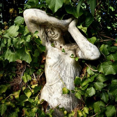 White statue of a Grecian woman covered in ivy as part of memorial garden ideas