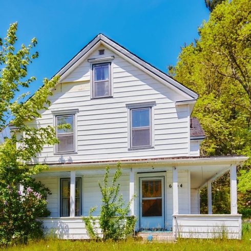 A two-storey house with white siding and a wrap-around porch