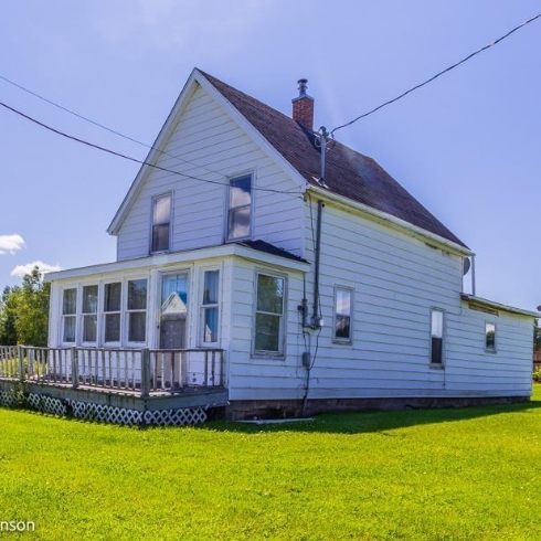 A one-and-a-half storey house with white siding, a large enclosed front porch, and brown shingles on a corner lot