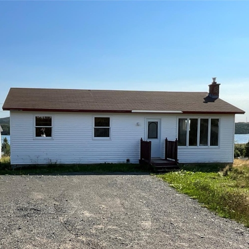 A one-storey bungalow by the water with white siding, brown shingles and a small front porch