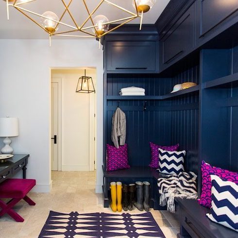 Beautiful blue entryway and mudroom designed by Sarah Baeumler with built-in shelves and cabinets, bold wall art, bright pillows, blue wallpapered feature wall and a blue rug as part of a home reno trends story for Home Network