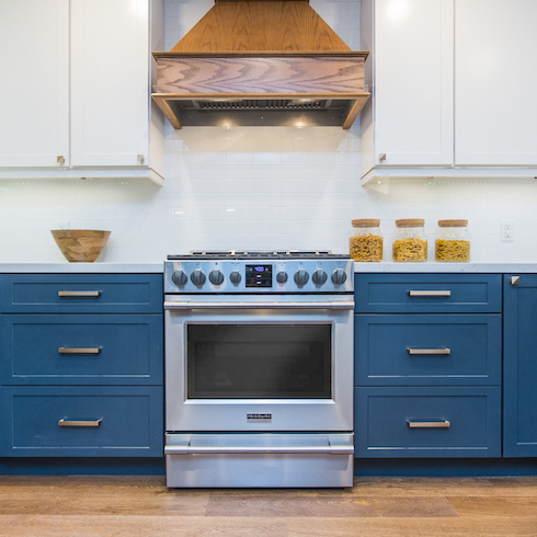 Bryan and Sarah Baeumler designed this beautiful kitchen featuring white upper cabinets and tranquil blue lower cabinets, wood floors and a wooden stove hood, and a white tile backsplash as part of a home reno trends story for Home Network