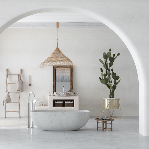 Modern white bathroom with a marbled white bathtub, potted cactus Plant, industrial floor lamp, large woven grass chandelier and wooden towel ladder leaning against a white wall as part of a home reno trends story for Home Network