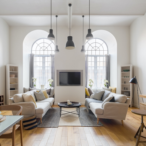 Contemporary living room with TV mounted between two large arched windows, two sofas with throw pillows, a large wool rug, a round coffee table and five round pendant lights hanging from the ceiling as part of a home reno trends story for Home Network