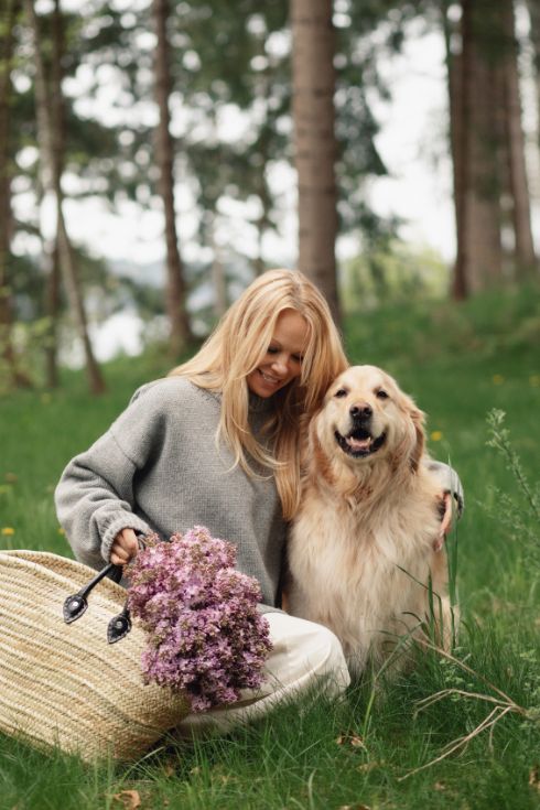 Pamela Anderson holding a bag with flowers and hugging a Golden Retriever dog