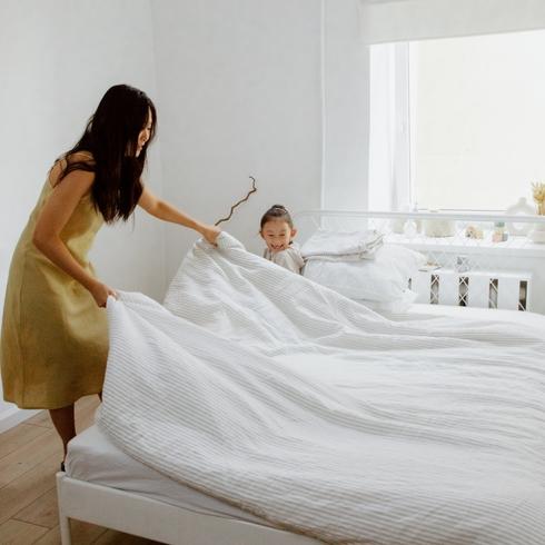 Mom and daughter making the bed in a white room