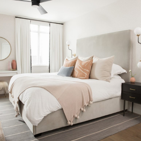 A bed with neutral, desert-toned linens and cushions beside a large window with white curtains