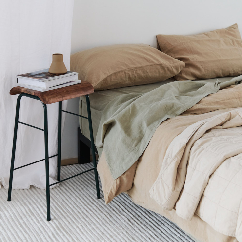 A Japandi style bed with neutral coloured linens and a small side table