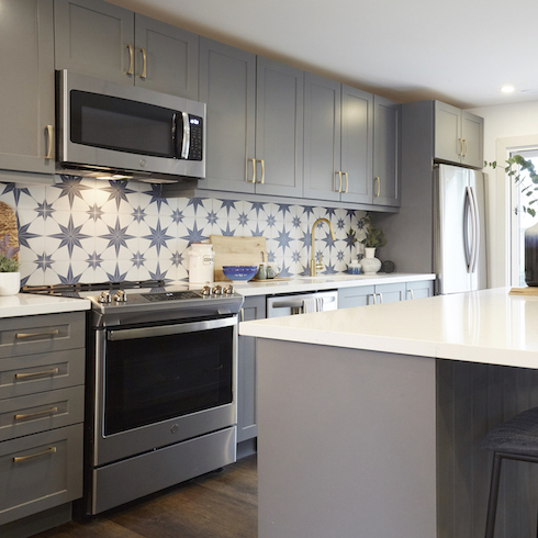 A beautiful kitchen for Home Network’s Scott’s Vacation House Rules features grey cabinets and blue star patterned tile backsplash