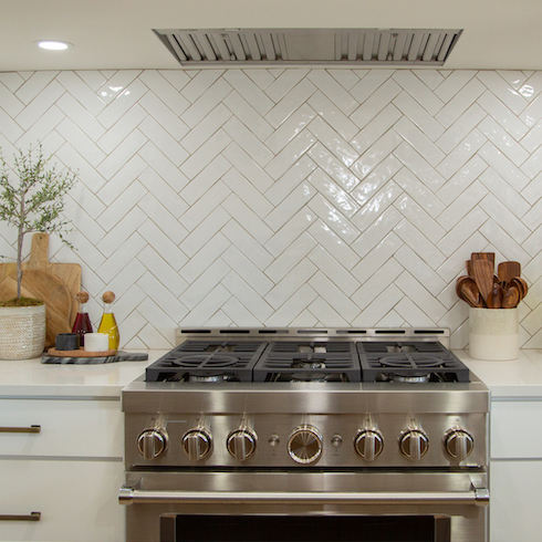 Beautiful white kitchen with white herringbone tile backsplash and a stainless steel gas range as featured on Home Network’s Making It Home With Kortney and Kenny