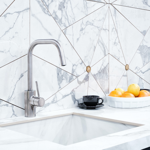 The interior of the modern kitchen is illuminated with a gray stone countertop with a luxury washbasin and mixer, fruit orange and a black cup and saucer