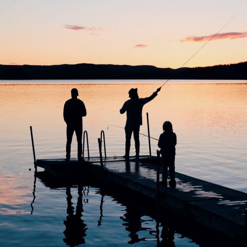 Three fishermen on a dock, silhouetted by the setting sun