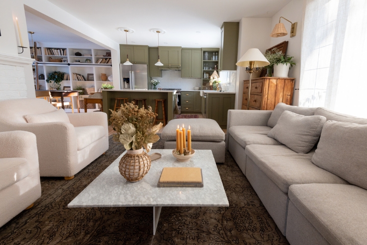 An open plan living room and kitchen with a large sofa, two armchairs and a marble-topped coffee table