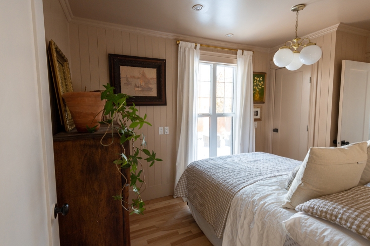 A bedroom with soft pink walls, a bed, a large dresser and a window