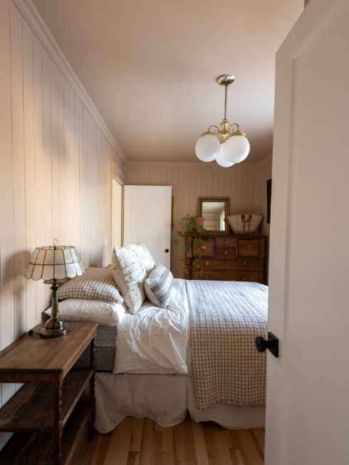 A bedroom with soft pink walls, a bed, side table, and large dresser on the far wall