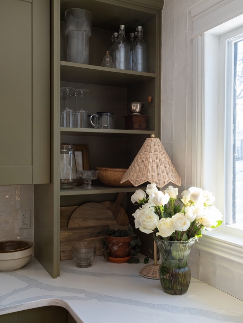 A kitchen corner with green cabinetry and open shelving