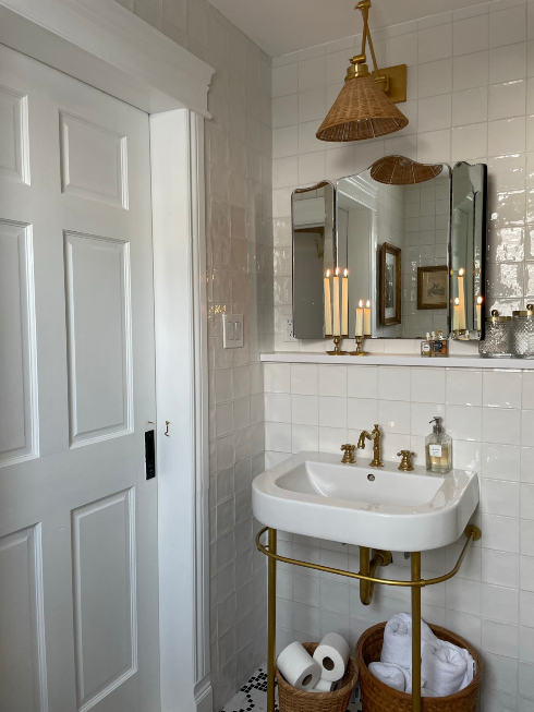 A bathroom sink with a mirror, overhead rattan pendant light and baskets of towels and toilet paper below the sink