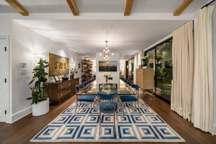 A dining room with large rectangular table, blue upholstered chairs, large windows and a beamed ceiling