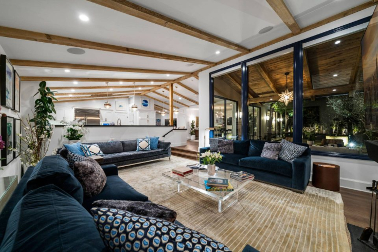 A recessed living room with large windows, beamed ceiling, sofas and a coffee table