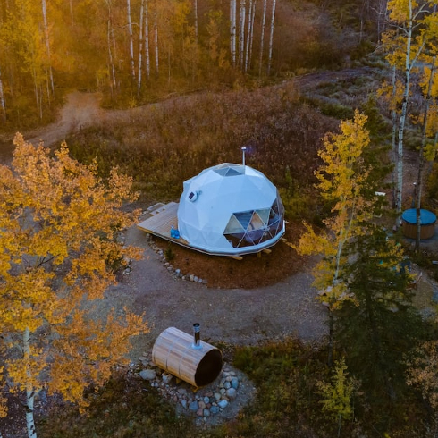 An overhead shot of a floating biodome Airbnb over a small peaceful lake