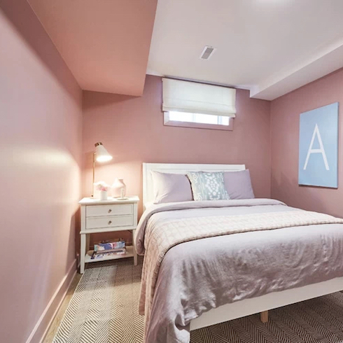 Basement bedroom from Extreme Makeover: Home Edition on Home Network is painted in all over petal pink with a double bed with pink and white bedding and a side table and area rug