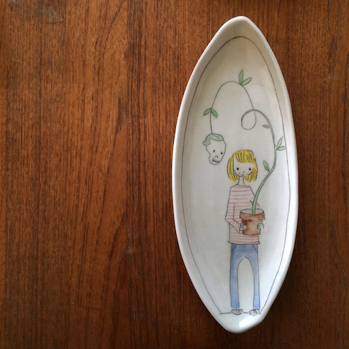 Oval dish by ceramic artist Carole Epp that features a girl holding a pot with a skull growing out of it